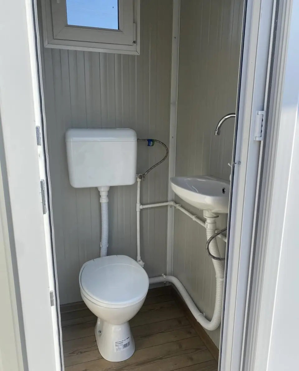 Inside a flushing portable toilet with a white tank toilet and small corner sink