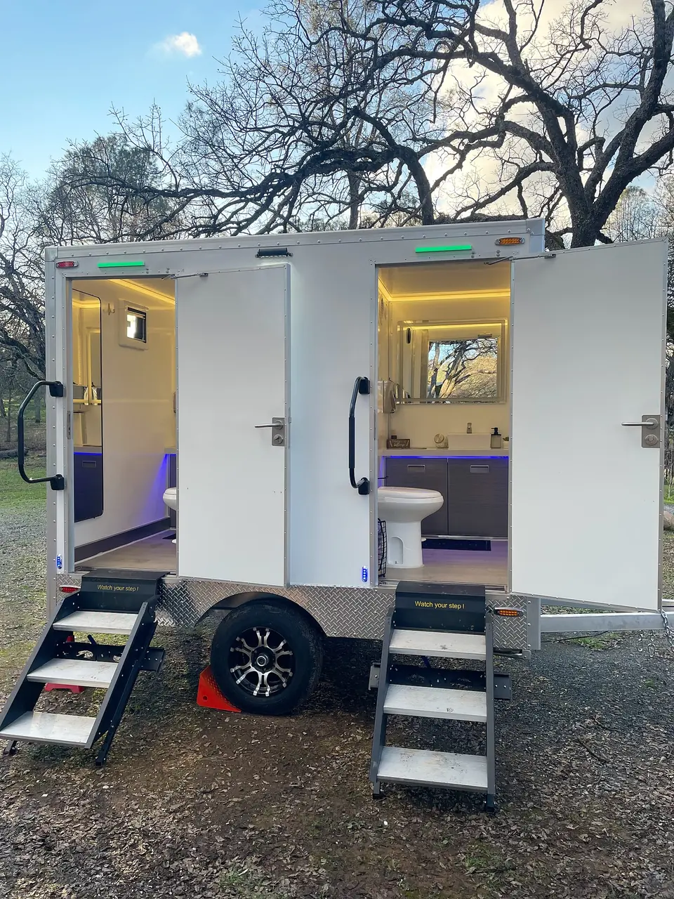 Two-door restroom trailer with lit interiors and steps at each door