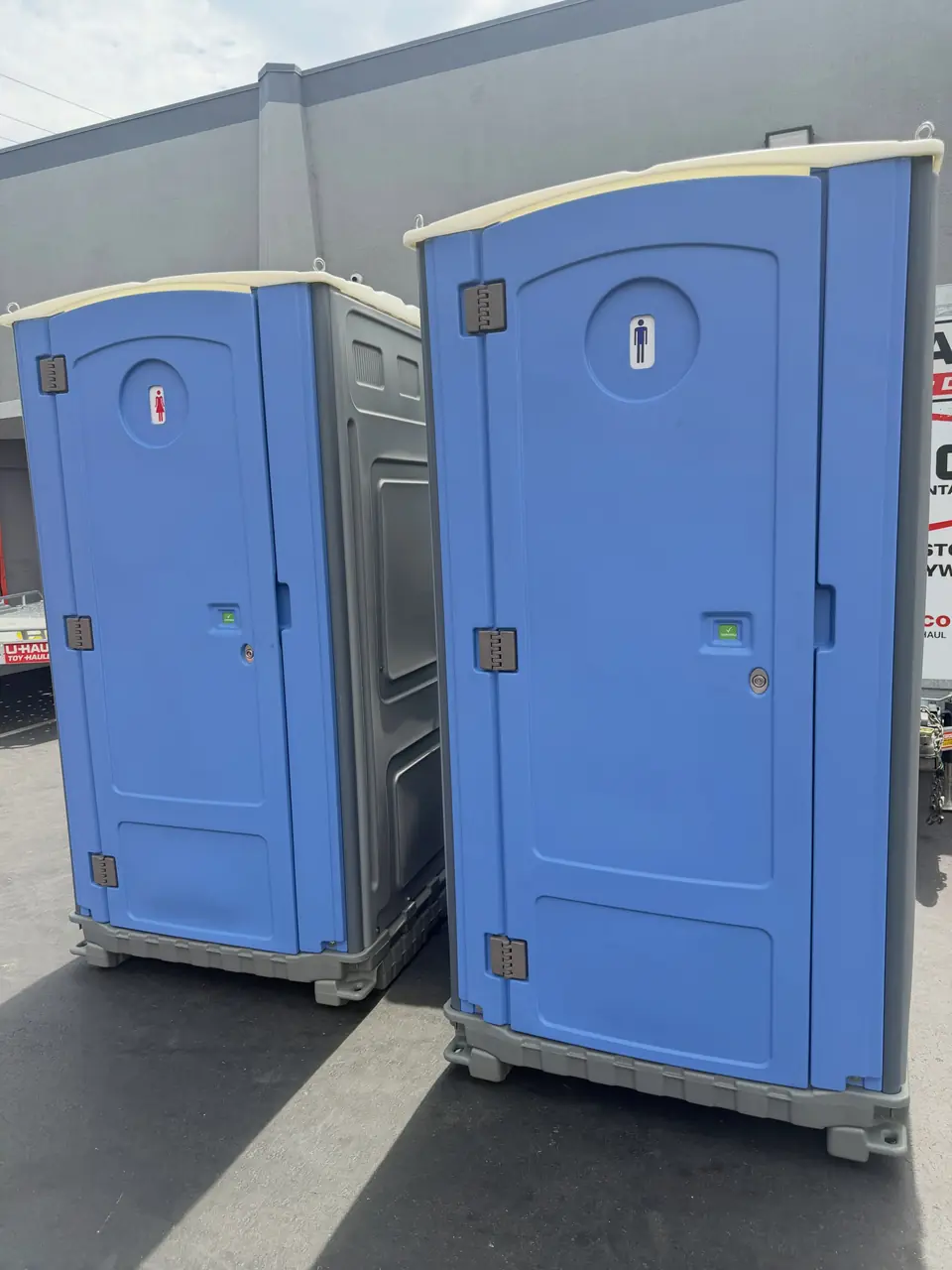 Two standard porta potties on a paved jobsite
