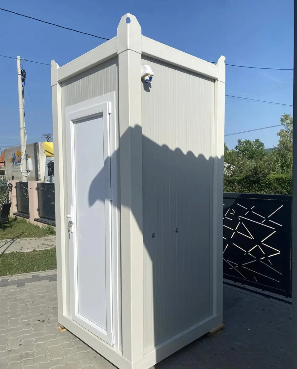 White flushing restroom cabin with a paneled door on a paved yard